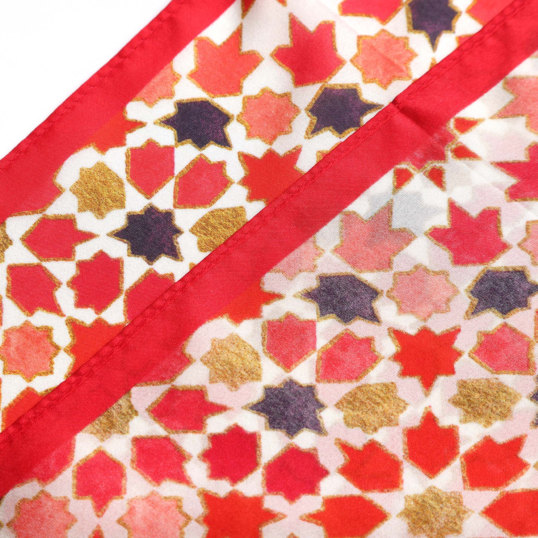 A close-up of the Small Square Scarf Alhambra, featuring a silk design with geometric star and floral patterns in red, gold, black, and pink—Islamic art-inspired with a bold diagonal red border.