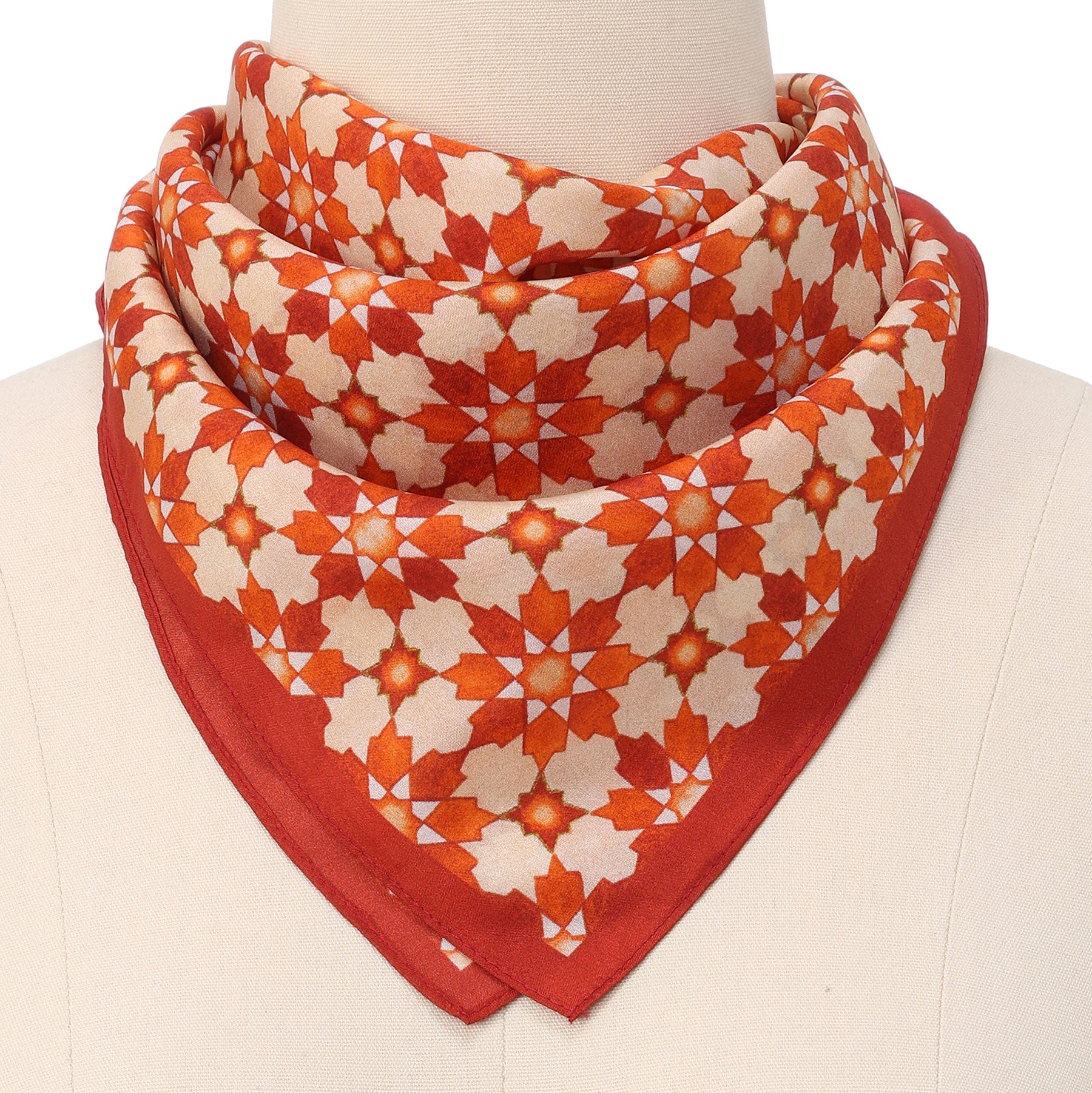 The Silk Neckerchief Orange Islamic Art Print, featuring a geometric star motif inspired by Islamic art, is neatly folded and displayed around a mannequin’s neck.