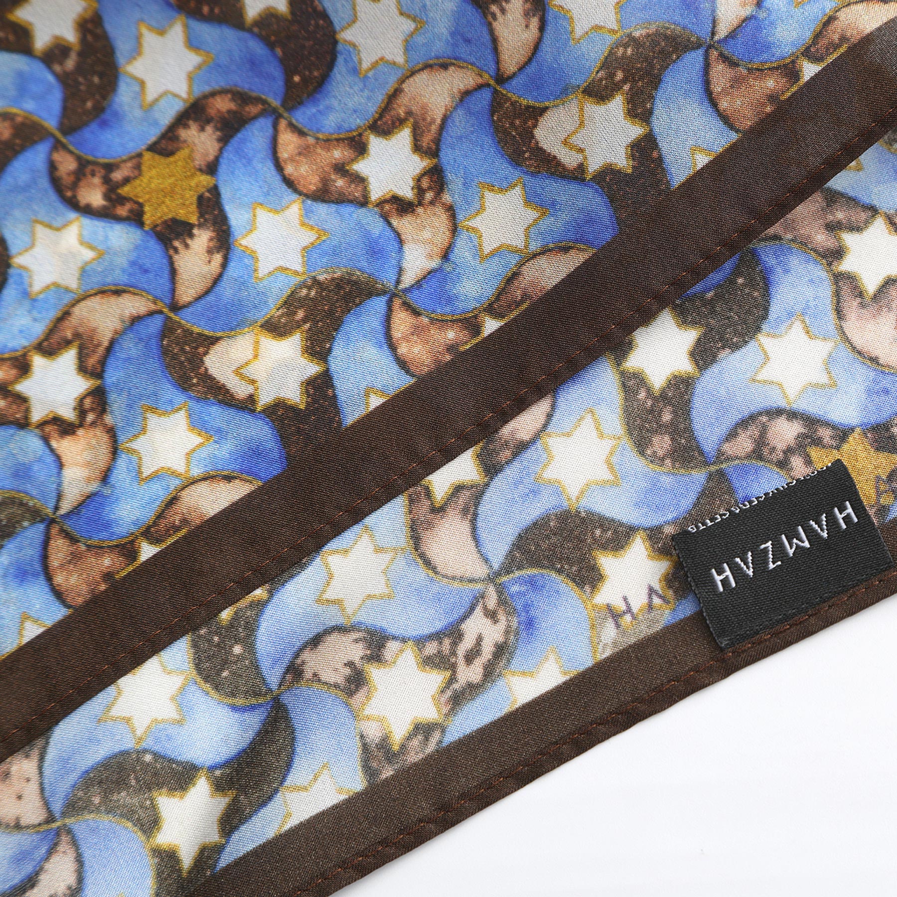The Silk Square Scarf for Women Brown features blue, brown, and cream wavy shapes with yellow and white stars, a brown border, an Islamic art-inspired print, and is finished with a black HAVZH tag.