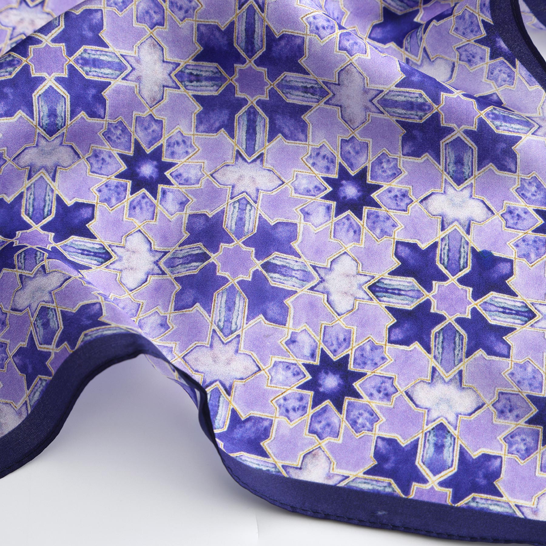 A close-up of the Square Silk Scarf for Women in purple, showcasing a geometric star pattern in blue and purple with gold outlines, interlocking shapes, and a dark purple border.