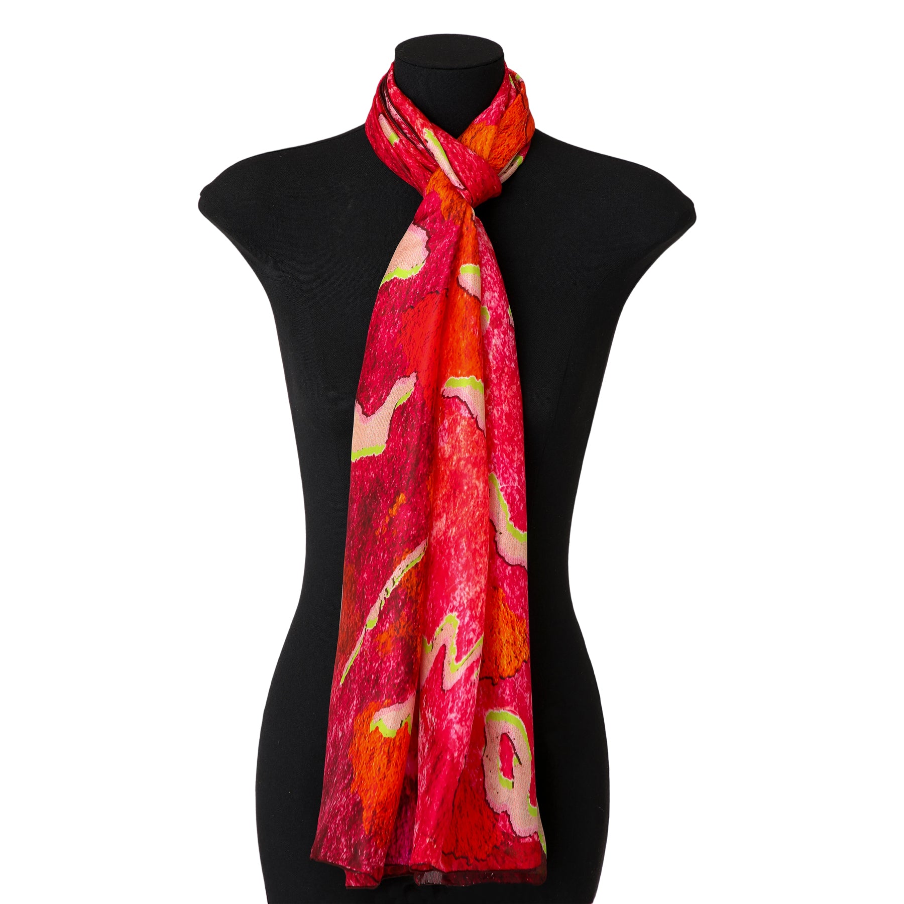 A Fuchsia Silk Scarf for Women featuring bright red, pink, and yellow patterns is tied around the neck of a black dress form mannequin.