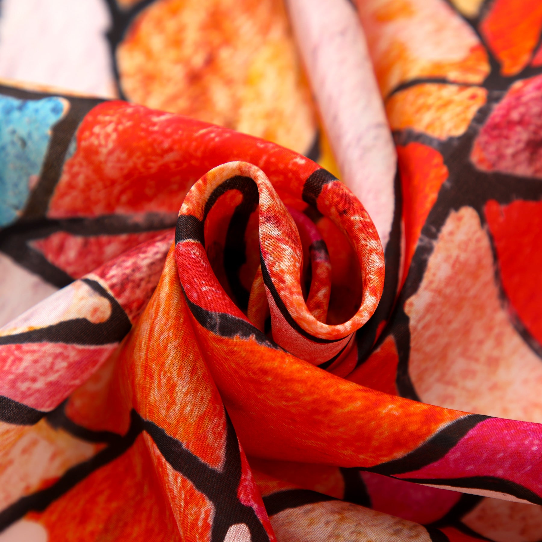A close-up of the Artistic Silk Scarf Vitrales de Luz reveals swirling folds of vibrant red, orange, pink, and blue outlined in black, evoking stained glass for a striking Mediterranean-inspired accessory.