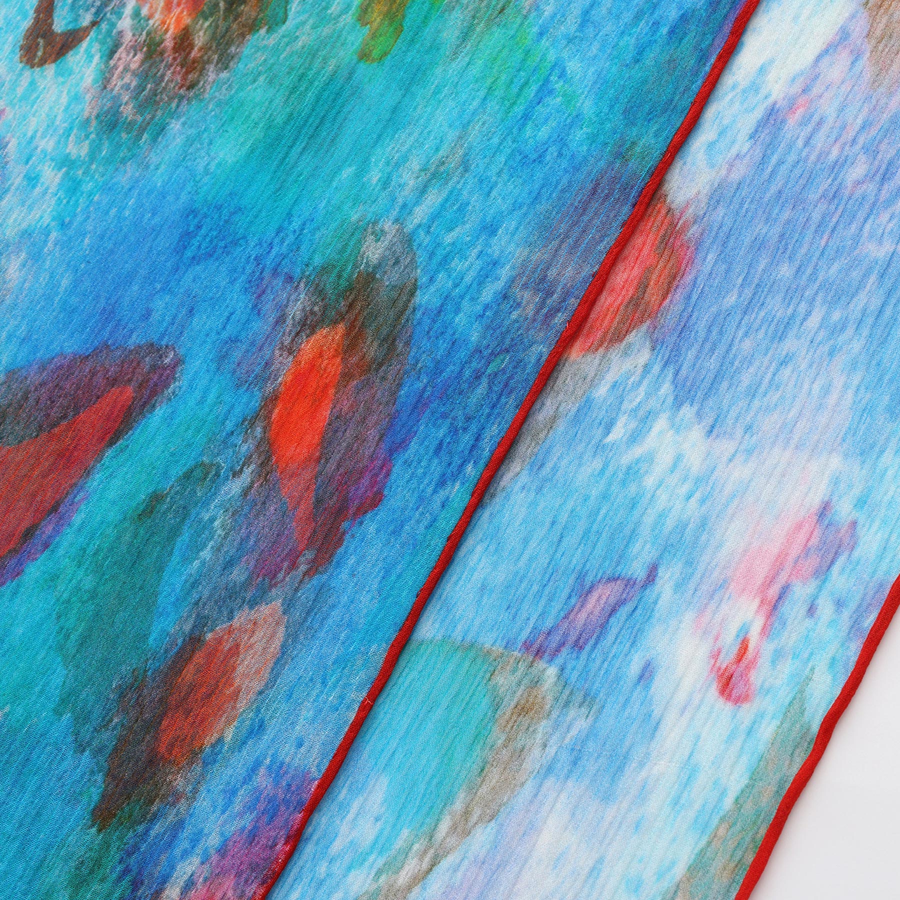 Close-up of the Multicolor Silk Scarf Mar Rojo, a Mediterranean silk accessory with vibrant blue fabric, abstract red, green, and orange patterns, thin red edging, and watercolor-style designs inspired by fish or organic shapes.