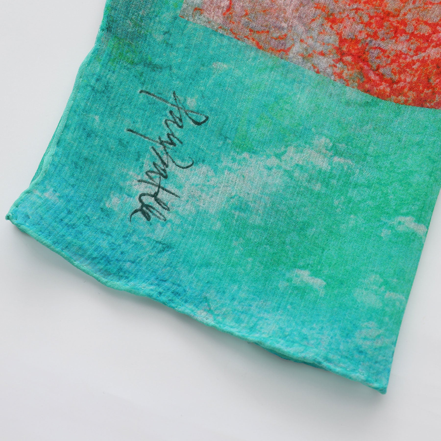 A close-up of the Multicolor Silk Scarf Fucsia Paradis in turquoise and red muslin silk with a textured pattern and black script, photographed on a white background—an elegant piece of wearable art.