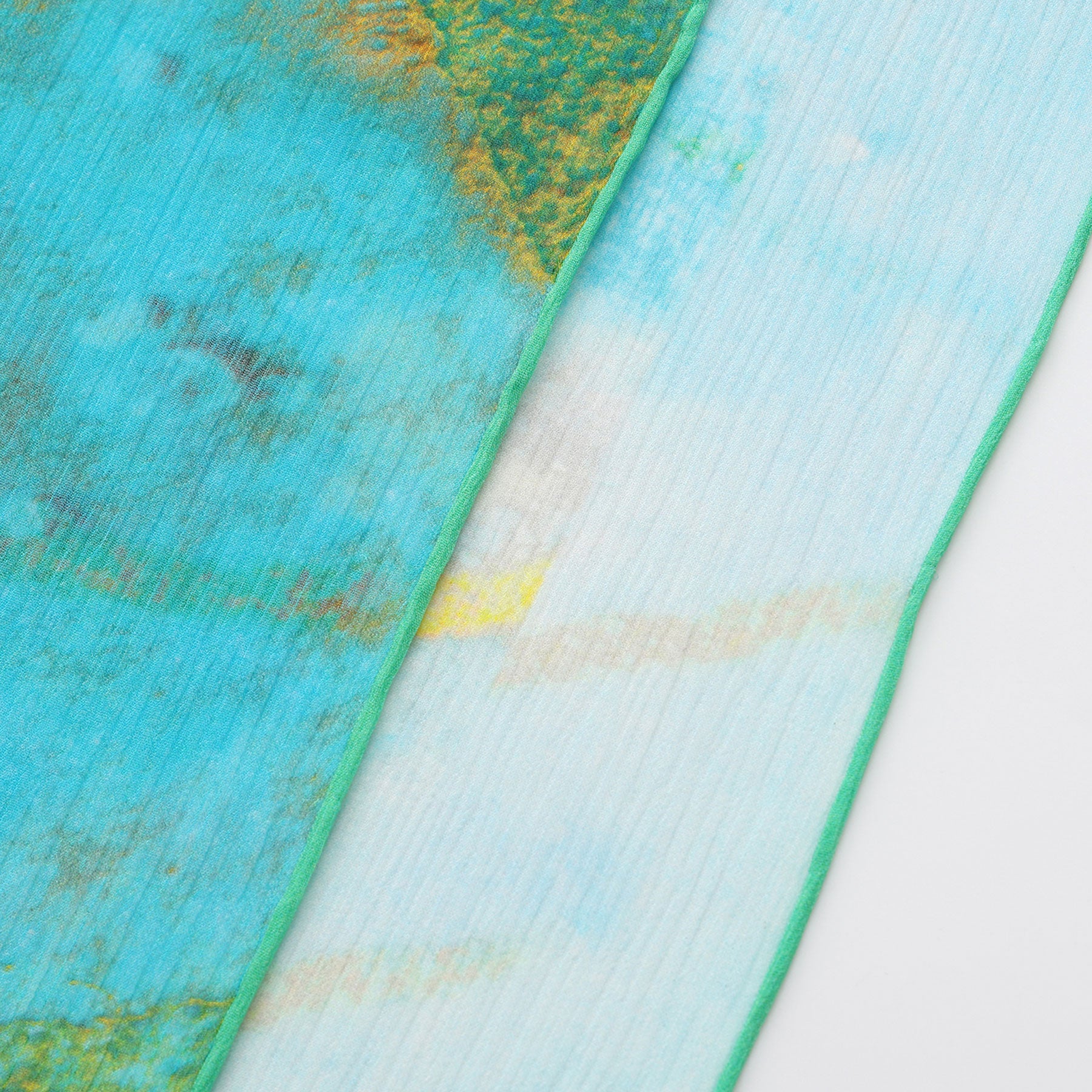 A close-up of the Multicolor Silk Scarf Oxido Marino, featuring overlapping blue and green sheer fabrics with yellow accents, a watercolor-style pattern, and green-stitched edges—an elegant muslin silk scarf on a white background.