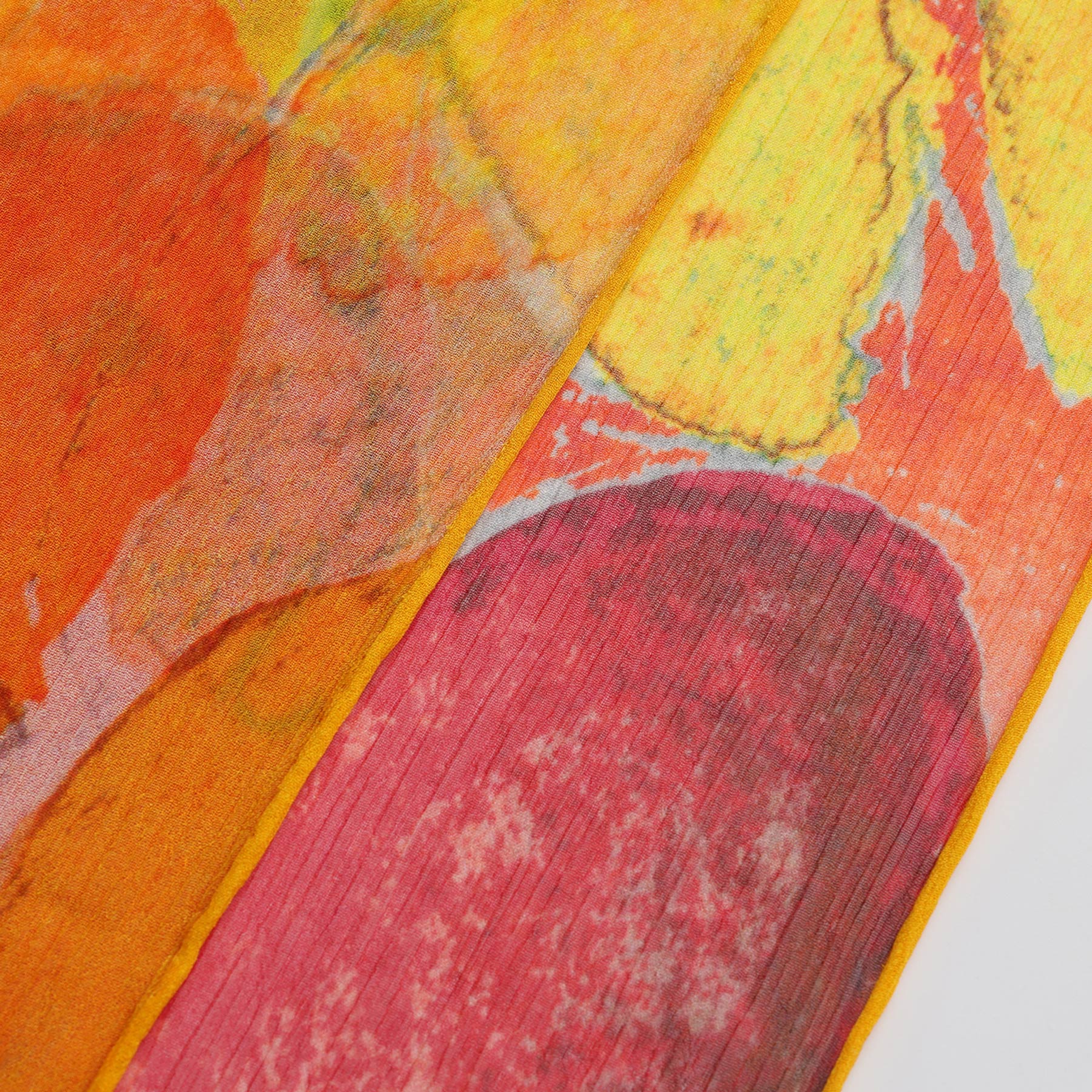 Close-up of the Multicolor Silk Scarf Demeter, showcasing bold orange, yellow, and red hues with organic shapes, visible texture, and a neatly finished yellow-edged seam—a unique piece of wearable art.