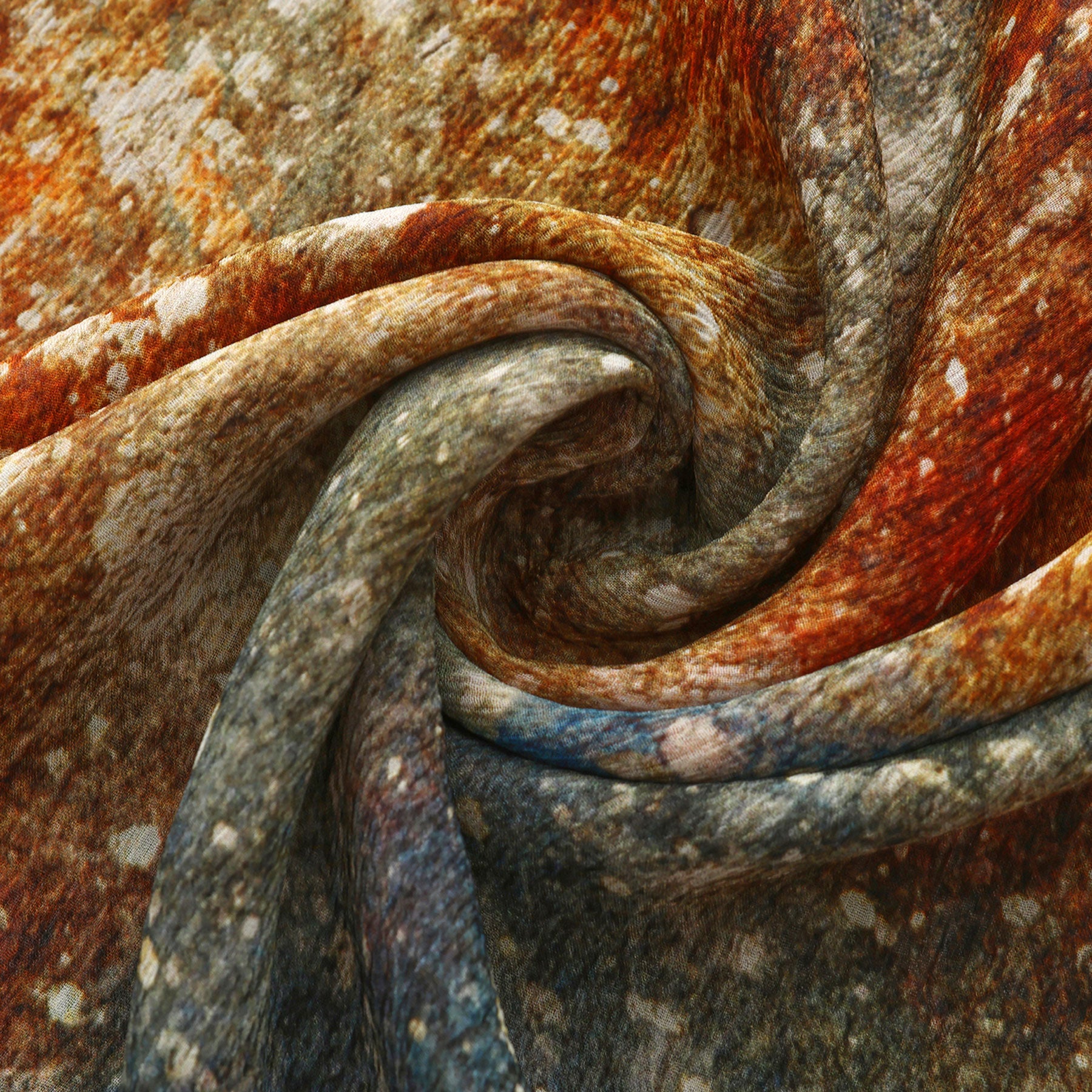 Close-up of the Multicolor Silk Scarf Polvo Cósmico, twisted into a spiral and displaying a mottled pattern in earthy brown, orange, and gray tones reminiscent of weathered stone.