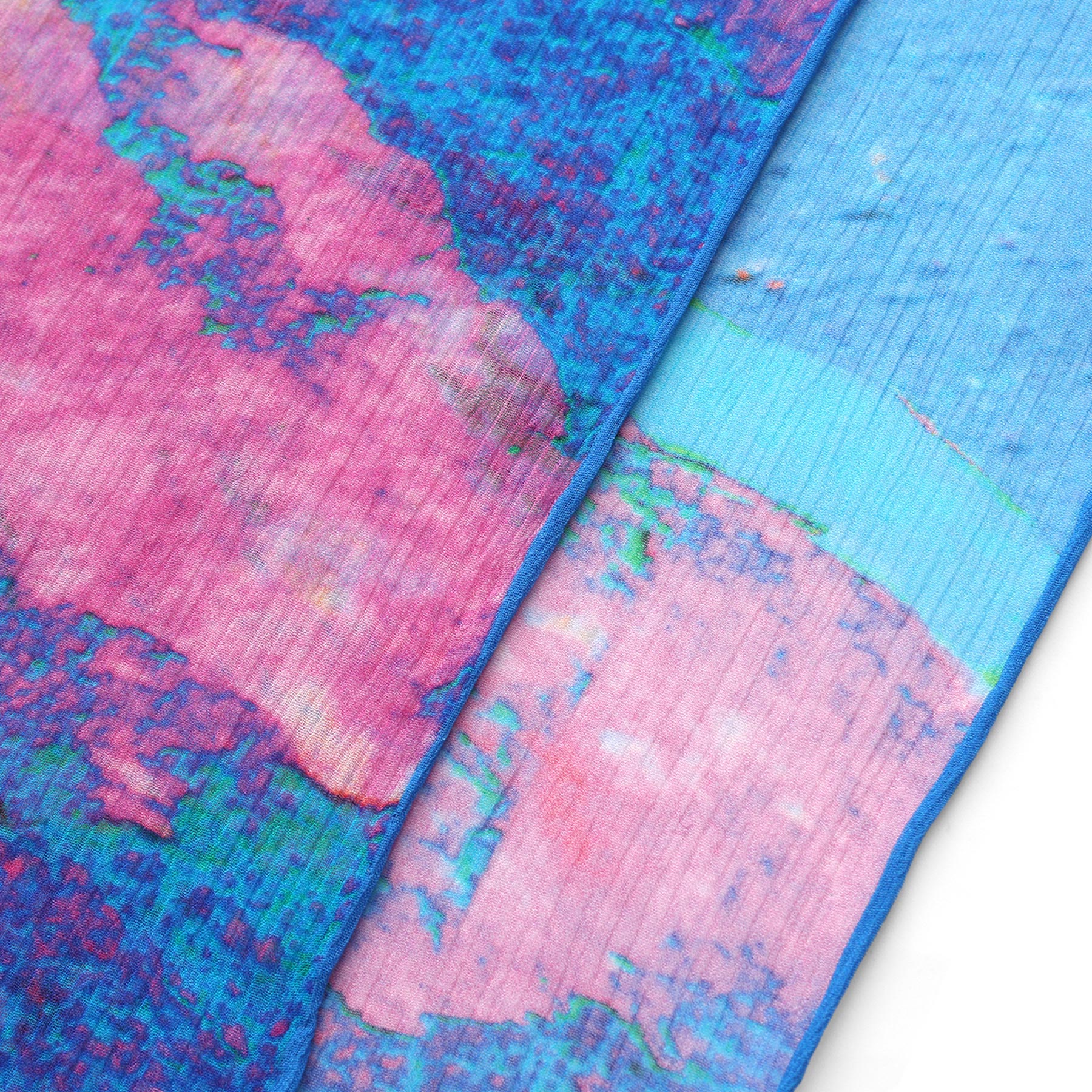Close-up of two overlapping fabrics with abstract pink, blue, and purple patterns—the Multicolor Silk Scarf Océano Fucsia displays rich textures and unique color gradients, making it a true piece of wearable art.