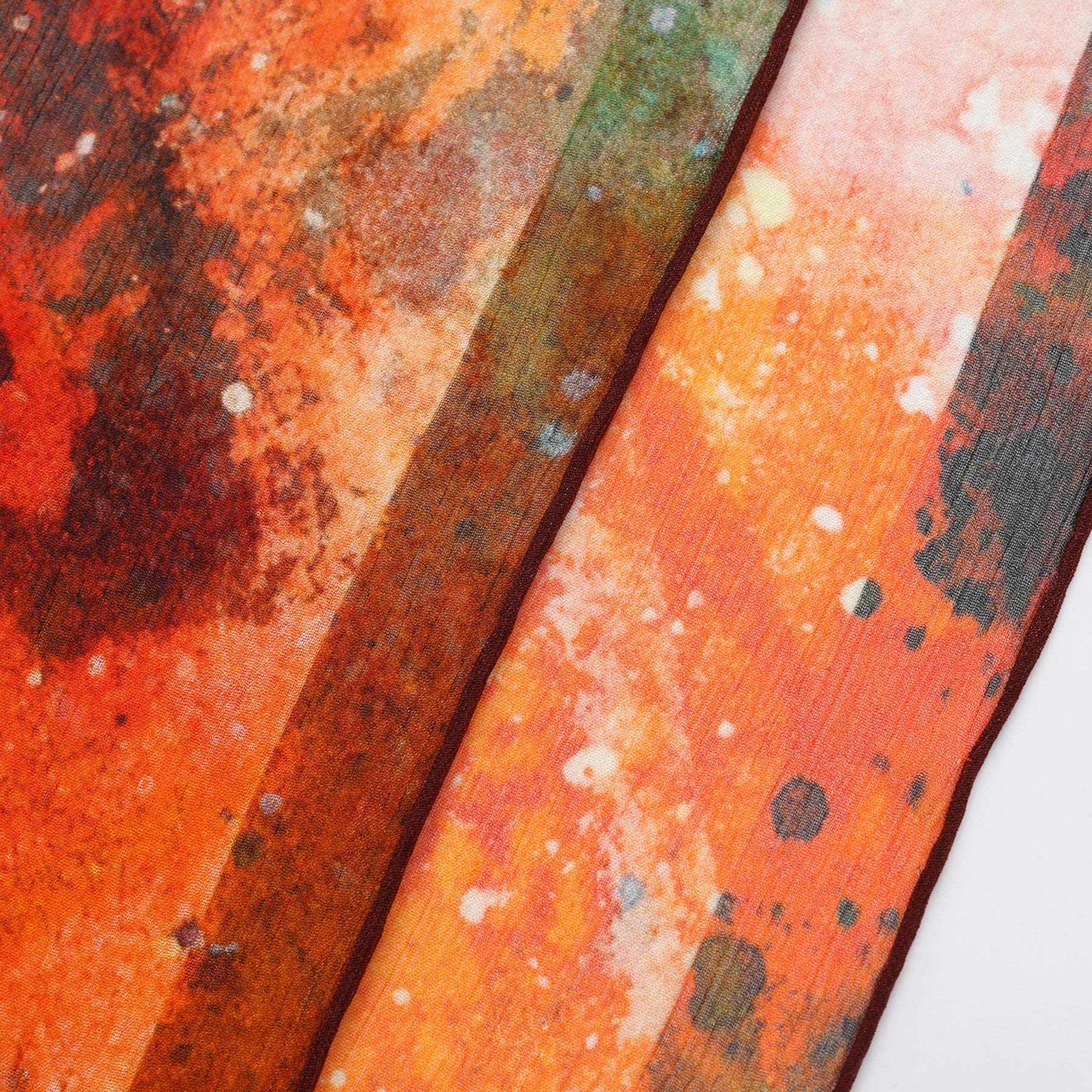 Close-up of the Multicolor Silk Scarf Cangrejos in orange and red muslin silk, showcasing abstract paint splatter and stripe patterns with dark spots and lighter areas for a textured, artistic look.