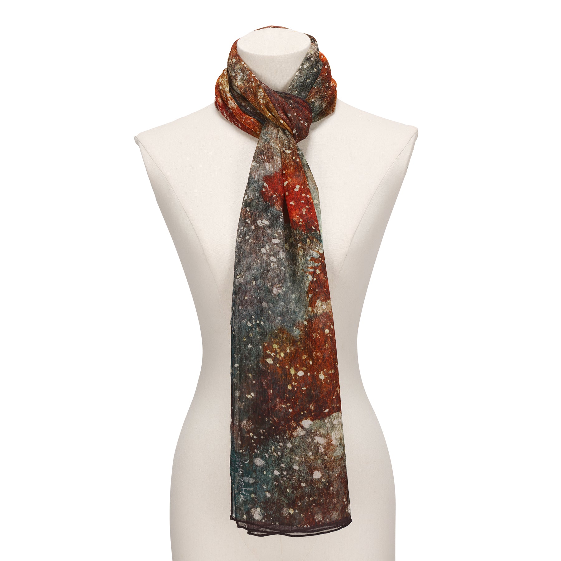 A white mannequin displays the Multicolor Silk Scarf Polvo Cósmico, a lightweight muslin silk accessory featuring an abstract autumnal pattern in red, orange, brown, and green, tied loosely around the neck as wearable artwork.