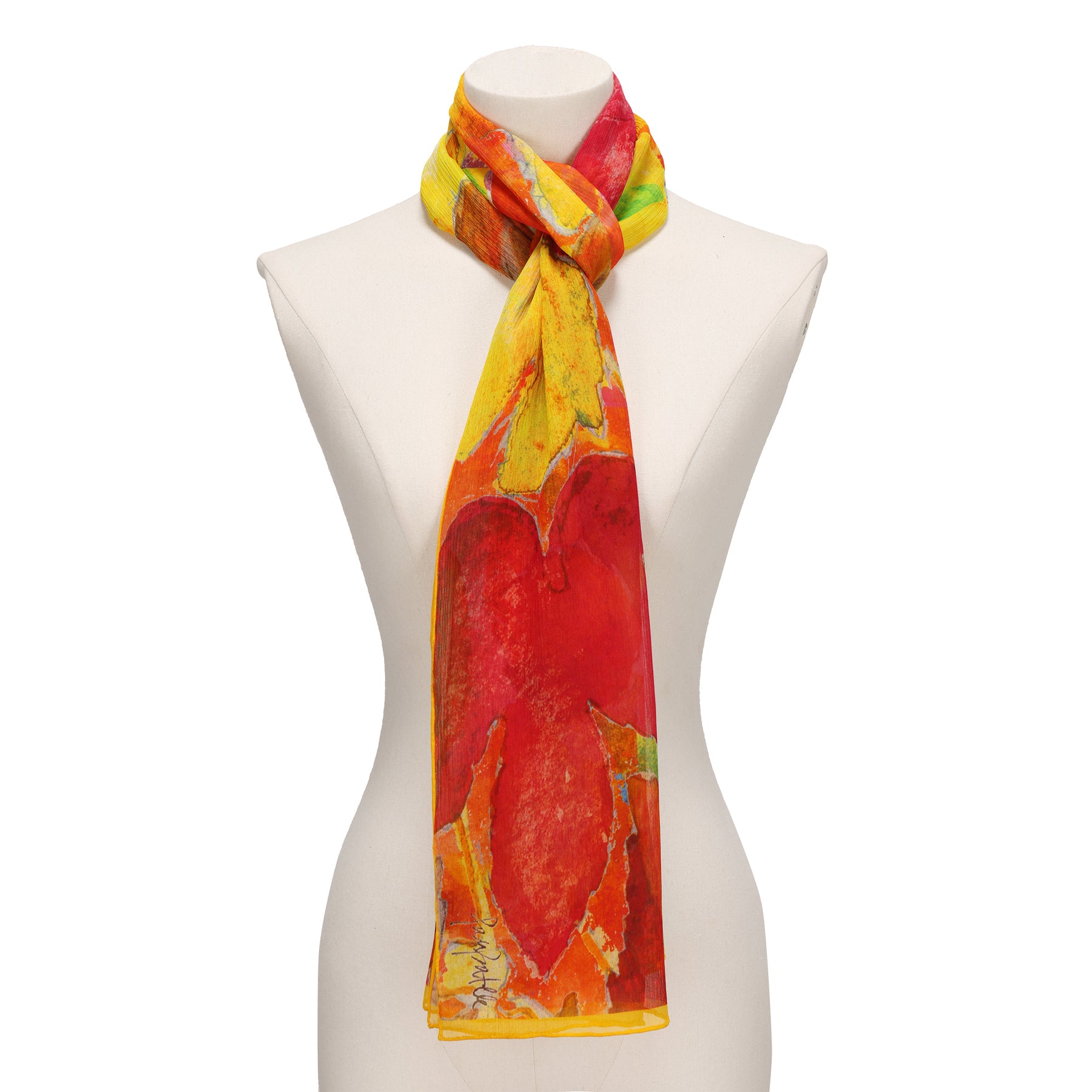 A mannequin showcases the Multicolor Silk Scarf Demeter, a vibrant muslin silk accessory with an abstract red, yellow, and orange design—tied loosely around the neck, it’s a true piece of wearable art.