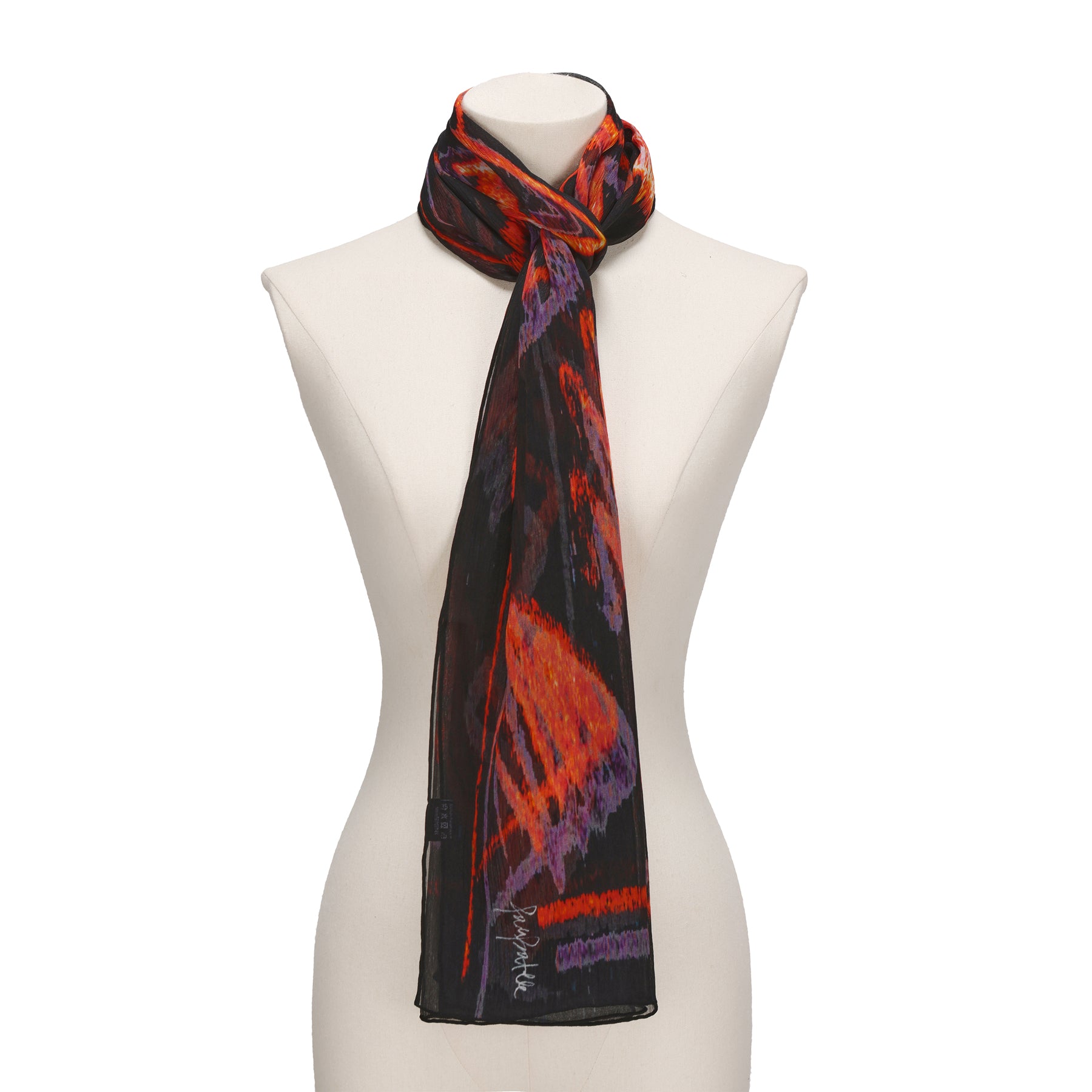 A mannequin displays the Black & Red Silk Scarf Anubis, a long muslin silk accessory with abstract red, black, orange, and purple patterns, draped and loosely knotted around the neck—a striking wearable artwork.