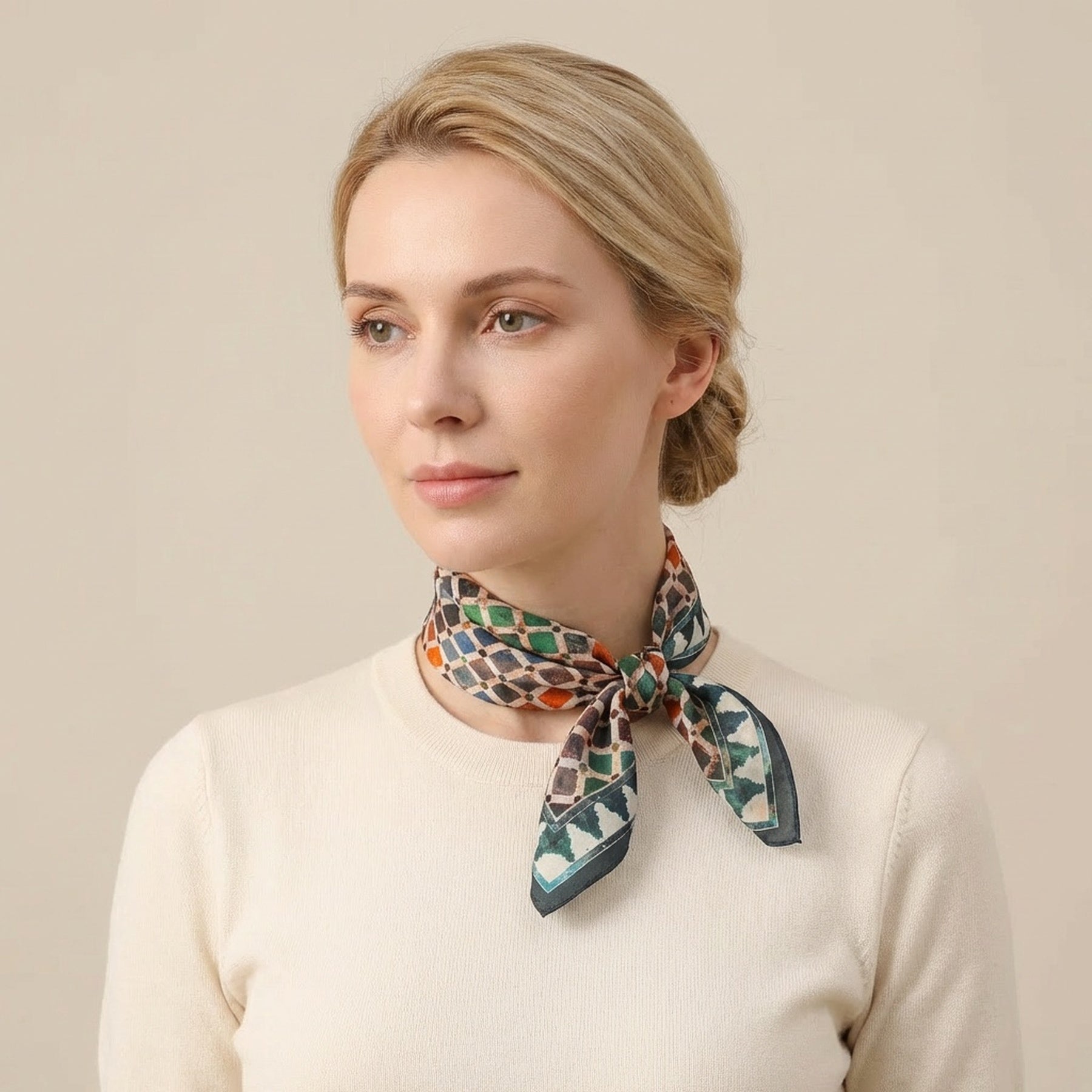 A woman with blond hair in a low bun wears a cream sweater and the Colorful Square Scarf Comares, inspired by Islamic art prints, tied around her neck as she looks to the side against a beige background.