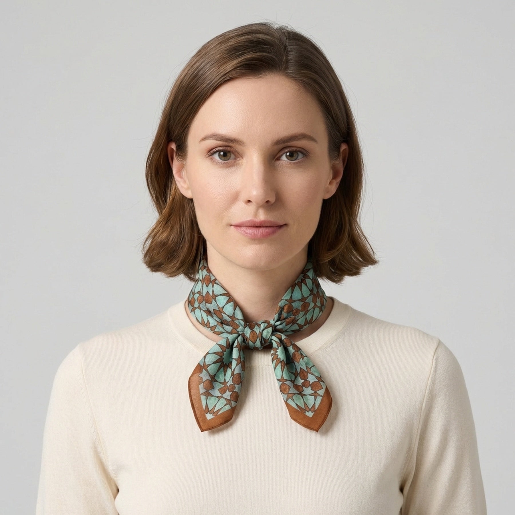 A woman with short brown hair, dressed in a cream top and the Brown Silk Neckerchief for Women, stands against a plain light gray background, looking directly at the camera with a neutral expression.