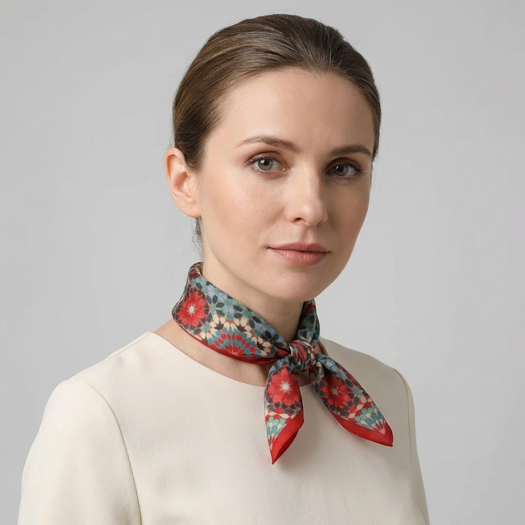 A woman with light skin and brown hair tied back wears a cream top and the Colorful Silk Neckerchief around her neck, posed against a plain grey background.