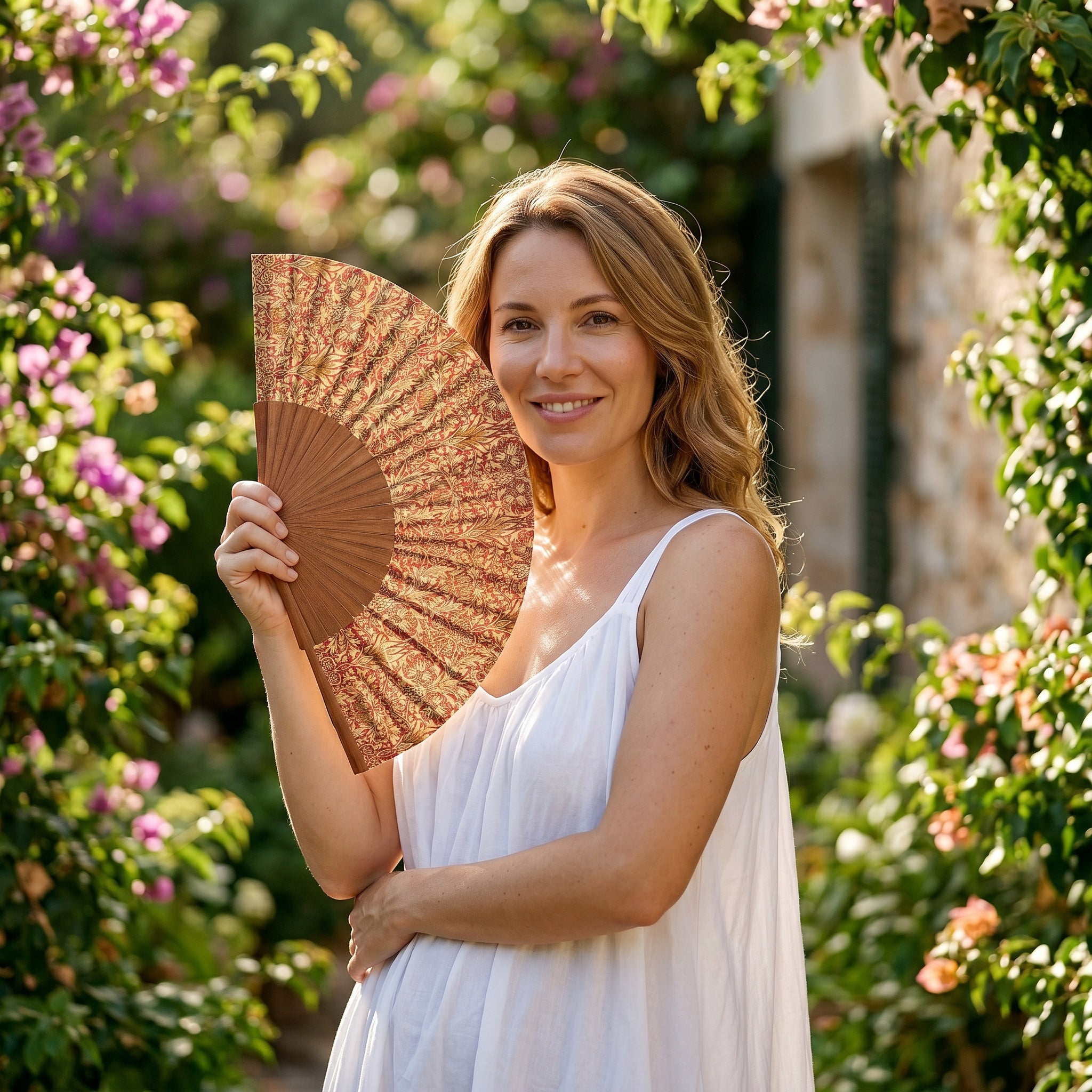 A woman in a summer outfit holding the open William Morris Print Hand Fan Renacentista with its William Morris botanical print in red and gold.