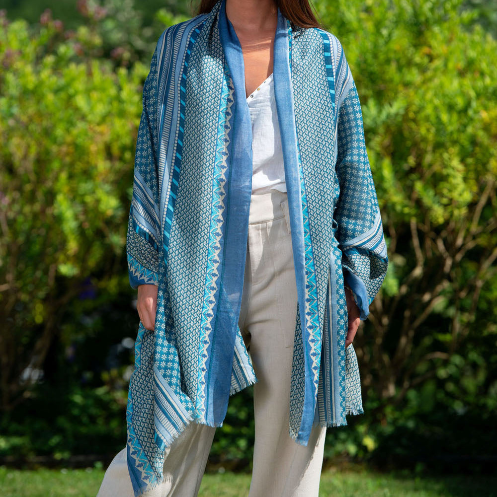 Model wearing a blue and white wool and silk scarf with an intricate geometric pattern. The lightweight fabric drapes elegantly over the shoulders, creating a refined and effortlessly chic look.