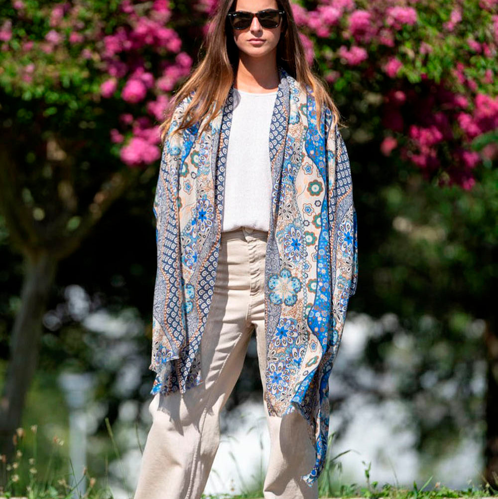 Stylish woman wearing a bohemian blue silk scarf with intricate floral and geometric designs, draped elegantly over a casual outfit. A timeless and versatile fashion accessory.