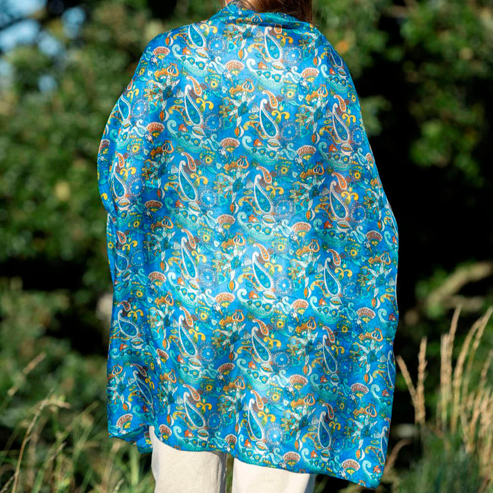 Back view of a luxurious blue silk scarf with intricate paisley and Islamic-inspired patterns, elegantly draped over a model outdoors.