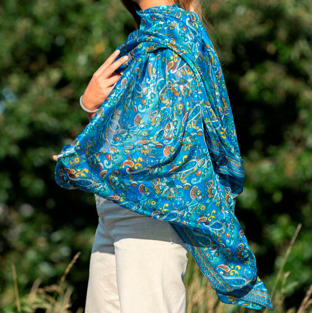 Elegant blue silk scarf with intricate paisley and Islamic-inspired patterns, worn by a model in an outdoor setting.