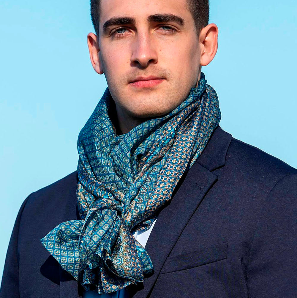 Man wearing an elegant blue silk scarf with intricate geometric patterns, styled with a suit against a clear blue sky.