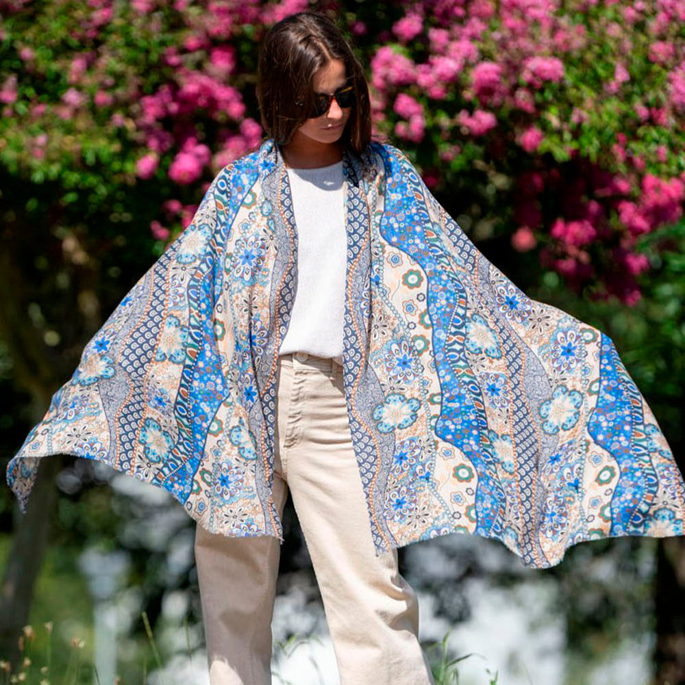 Blue silk and wool scarf with intricate floral and geometric patterns, standing against a vibrant backdrop of pink blossoms. A stylish and elegant statement piece.