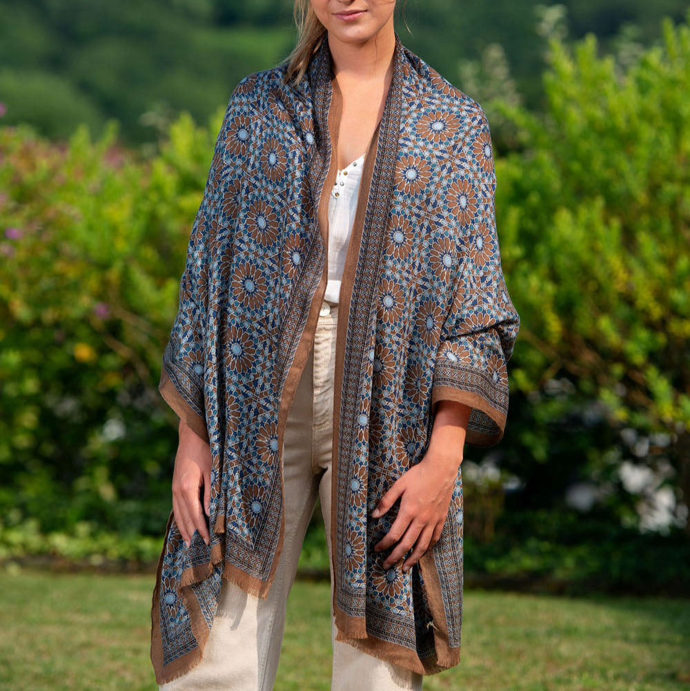 A model showcases a luxurious brown and blue silk scarf with an intricate mosaic pattern, elegantly tied at the front. The lightweight, flowing fabric adds a touch of refinement and versatility, perfect for elevating any outfit with an artistic and sophisticated charm.