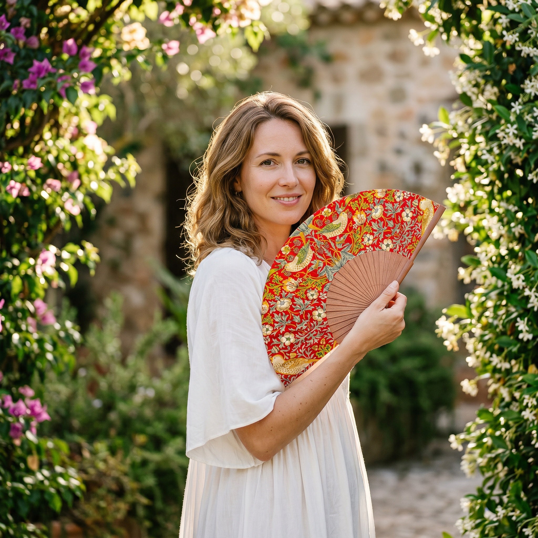 A woman in a summer outfit holding the open William Morris Print Hand Fan Birds with its William Morris Strawberry Thief print.