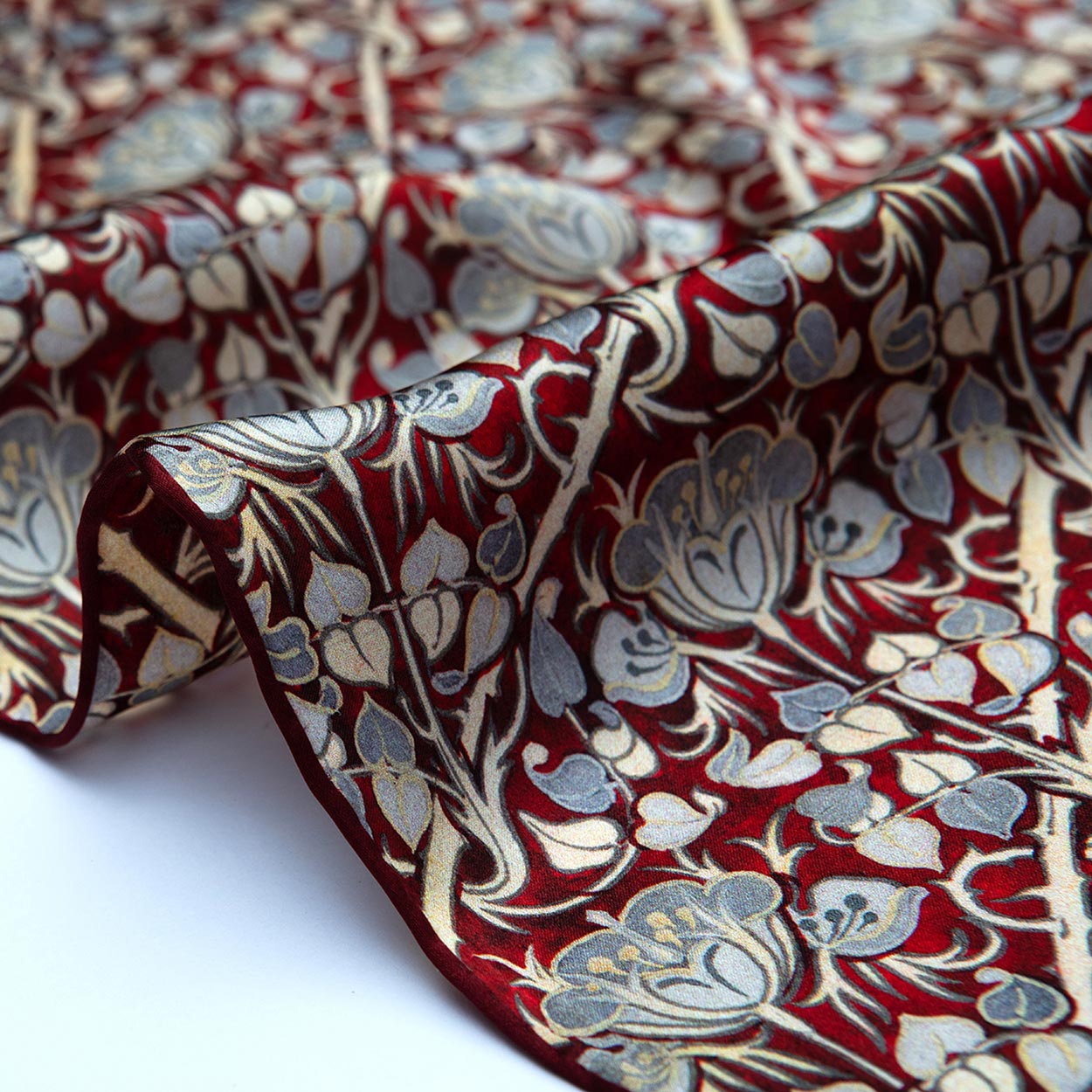 Swirled section of the burgundy roses scarf, emphasizing the ornate silver and gold motifs on the deep red background.