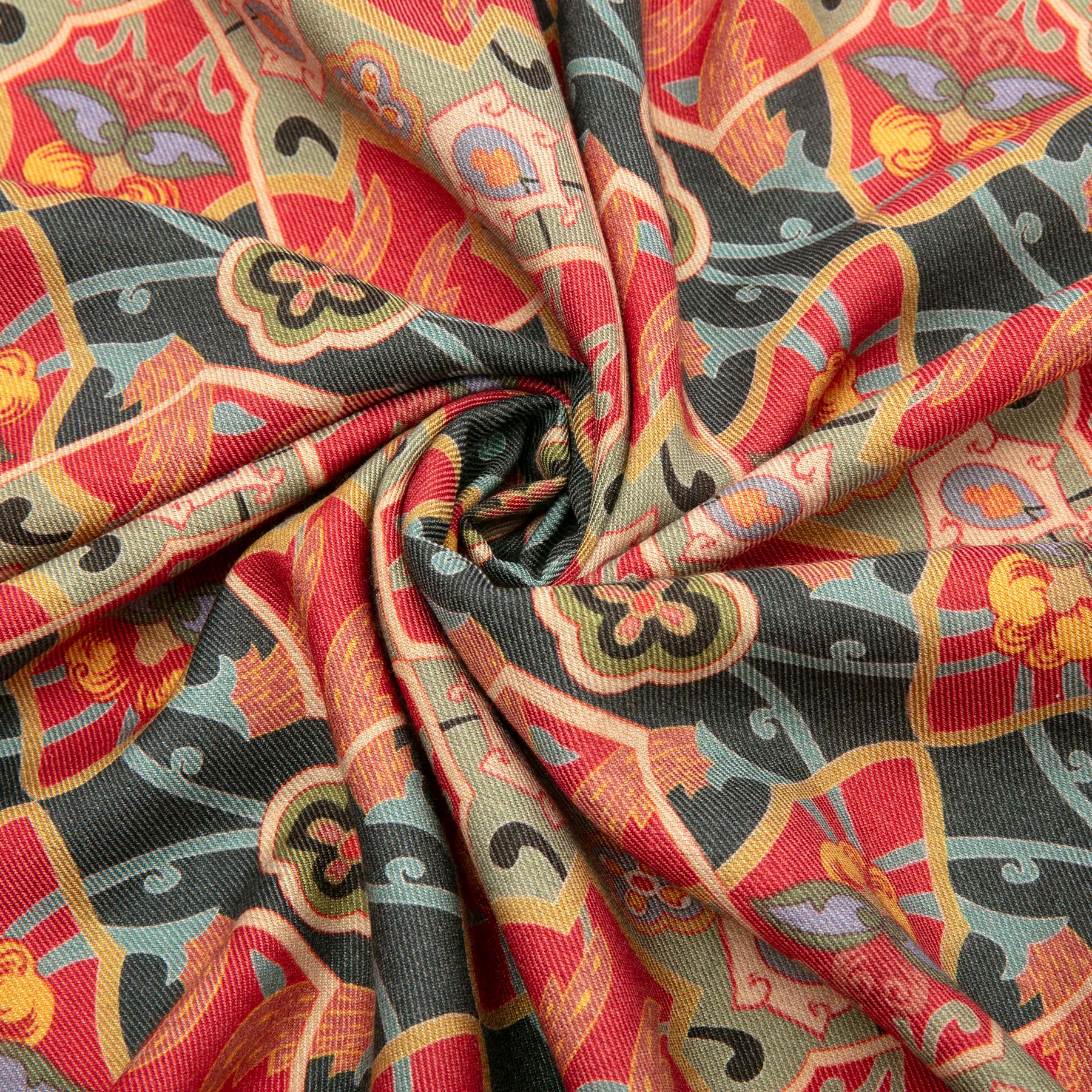 A close-up of Hamzahs Silk and Wool Red Scarf Rania, twisted into a spiral, displays a vivid mix of red, orange, yellow, and blue hues with abstract floral and geometric designs reminiscent of Islamic Art Print.