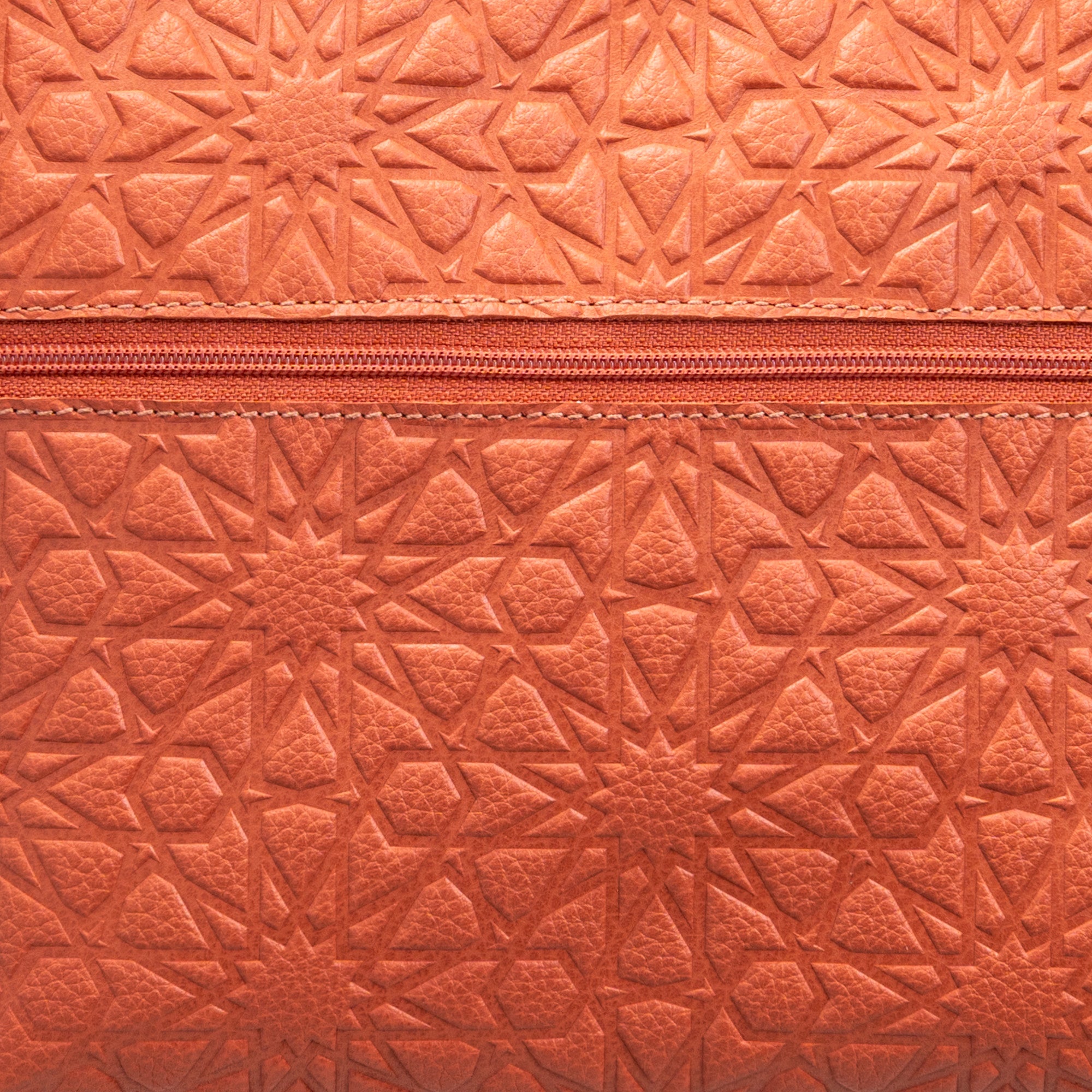 Close-up of the Orange Embossed Crossbody Bag with Islamic Design Pattern, showcasing its textured surface and a central horizontal zipper.