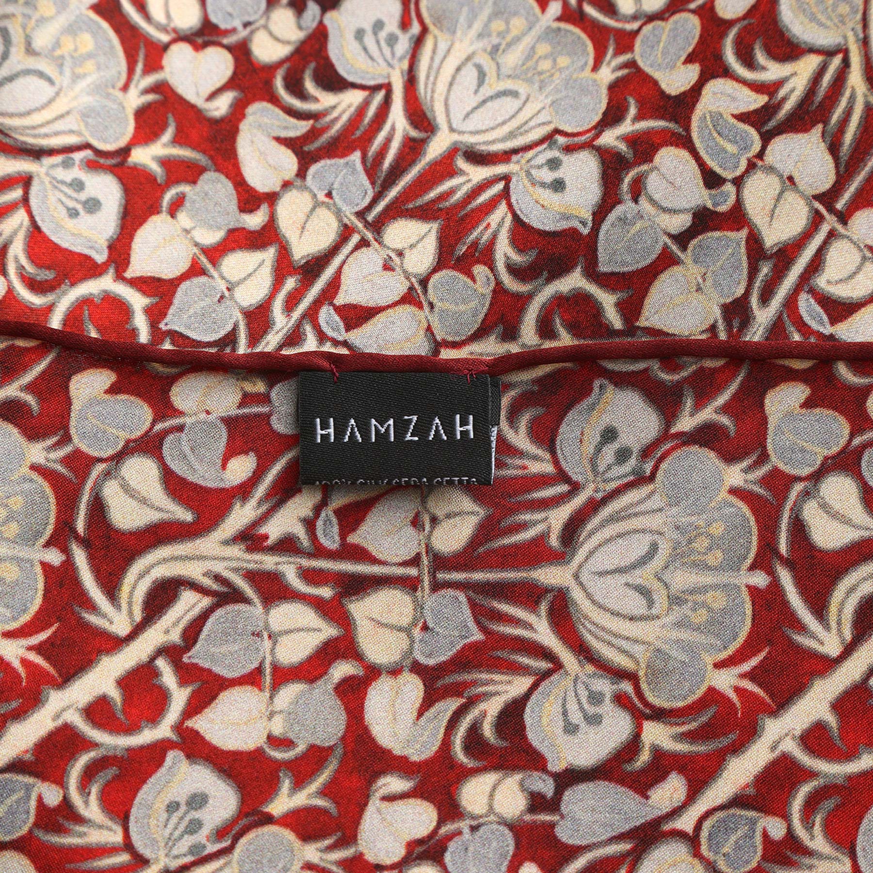 A rectangular black box with a window displays the Burgundy and Gray Silk Scarf with Roses Print Noisette. The brand name HAMZAH is at the top, and Wrap yourself in elegance is written at the bottom.
