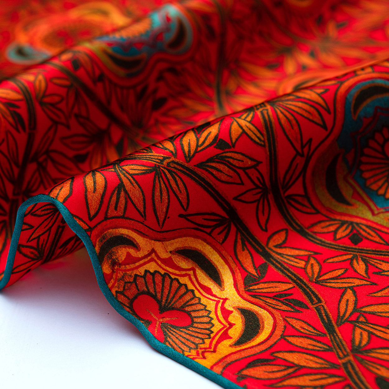 Swirled section of the red silk scarf emphasizing the intricate leaves and blooming shapes in orange, gold, and teal.