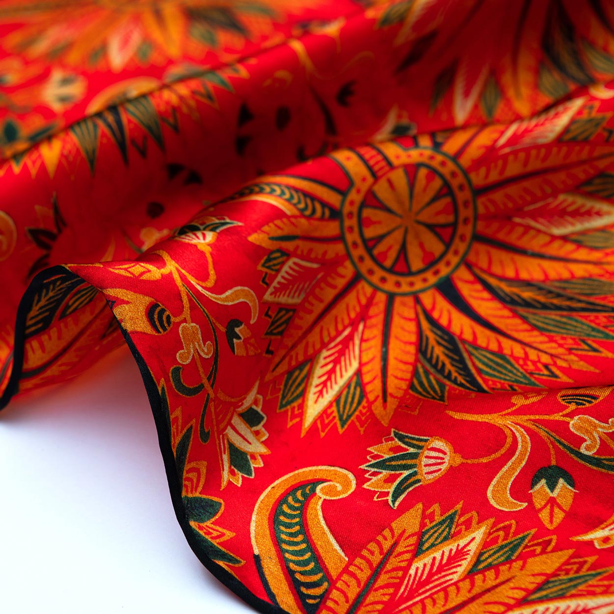 Zoomed-in image of the red silk scarf’s black edge, showcasing the elaborate golden and green floral elements against the richly colored fabric.