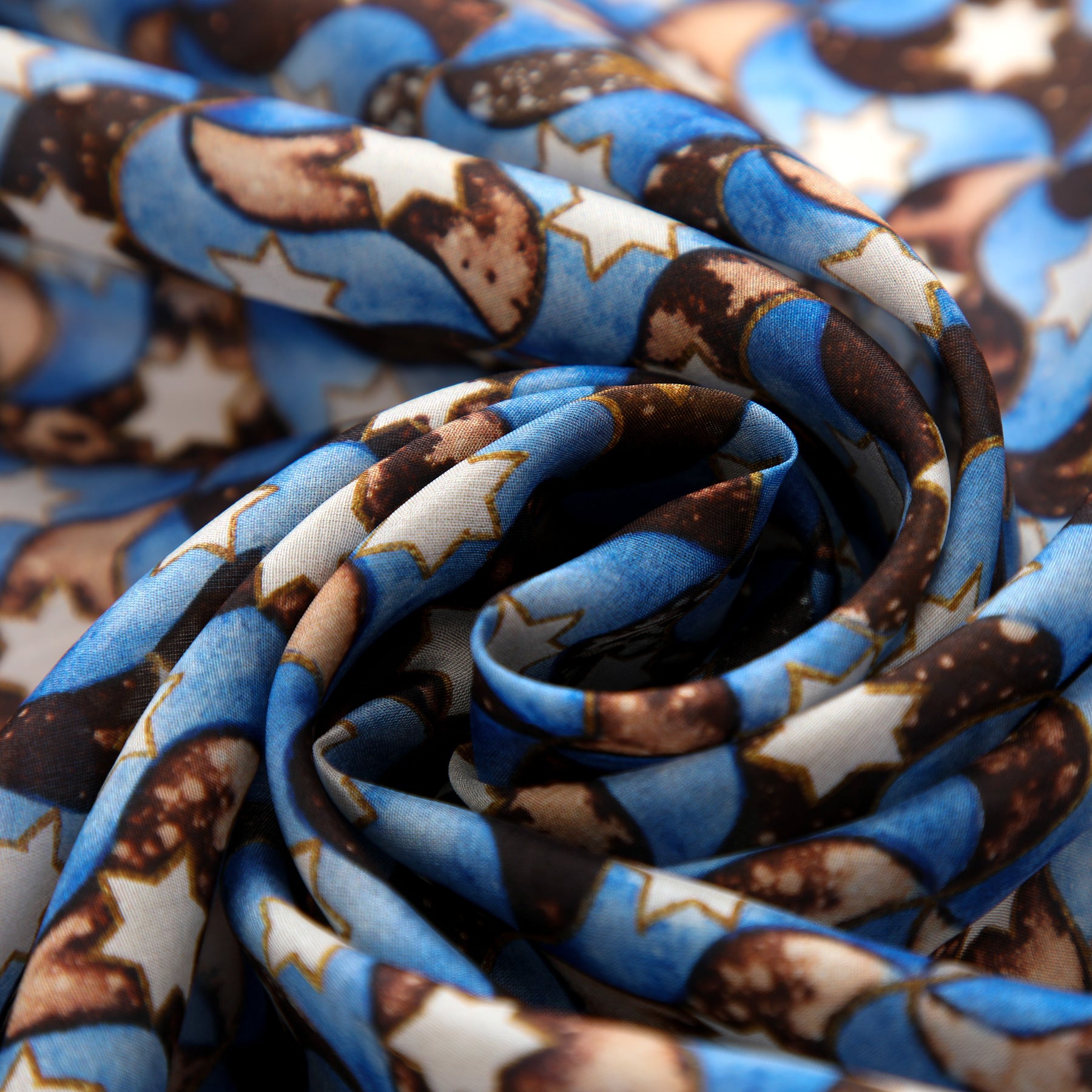 A close-up of the Silk Scarf Islamic Design Pajarita, in blue, brown, and white tones with star and moon motifs inspired by Islamic art, elegantly gathered into soft swirling folds.