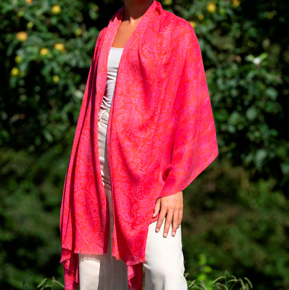 Model showcasing a luxurious pink wool and silk scarf with an intricate paisley pattern, elegantly draped over one shoulder. The soft, flowing fabric catches the sunlight, highlighting its vibrant color and delicate texture.