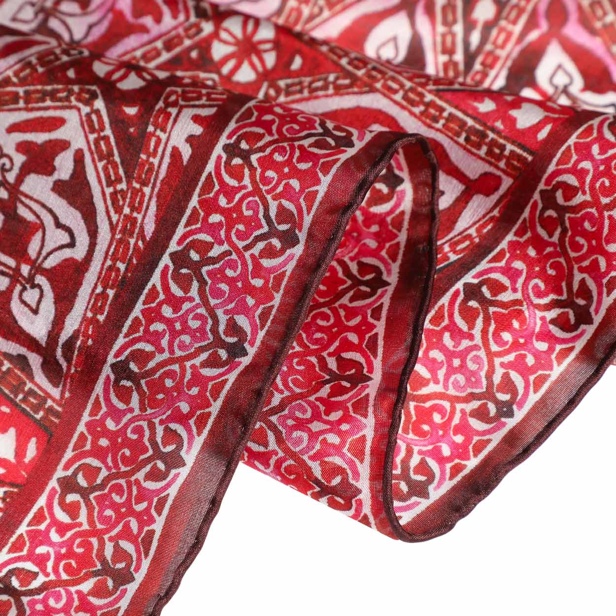 Close-up of the hand-stitched hem of a red silk scarf with intricate Andalusian-inspired Islamic patterns. The fine details highlight the craftsmanship and luxurious texture of the fabric.