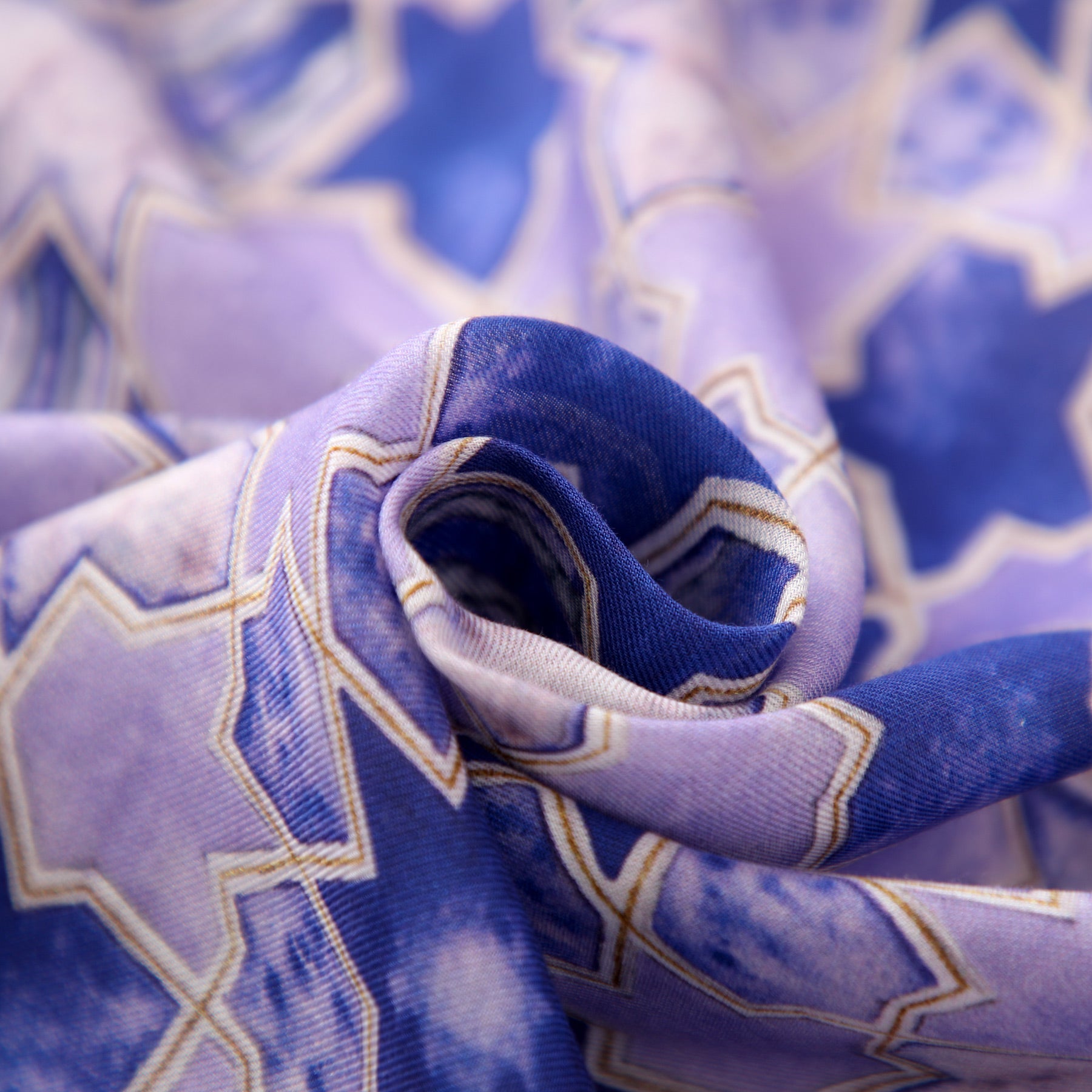A close-up of the Purple Scarf for Women - 100% Modal shows blue and purple geometric patterns with gold outlines, softly folded in a swirl for an elegant, timeless look inspired by intricate Islamic designs.