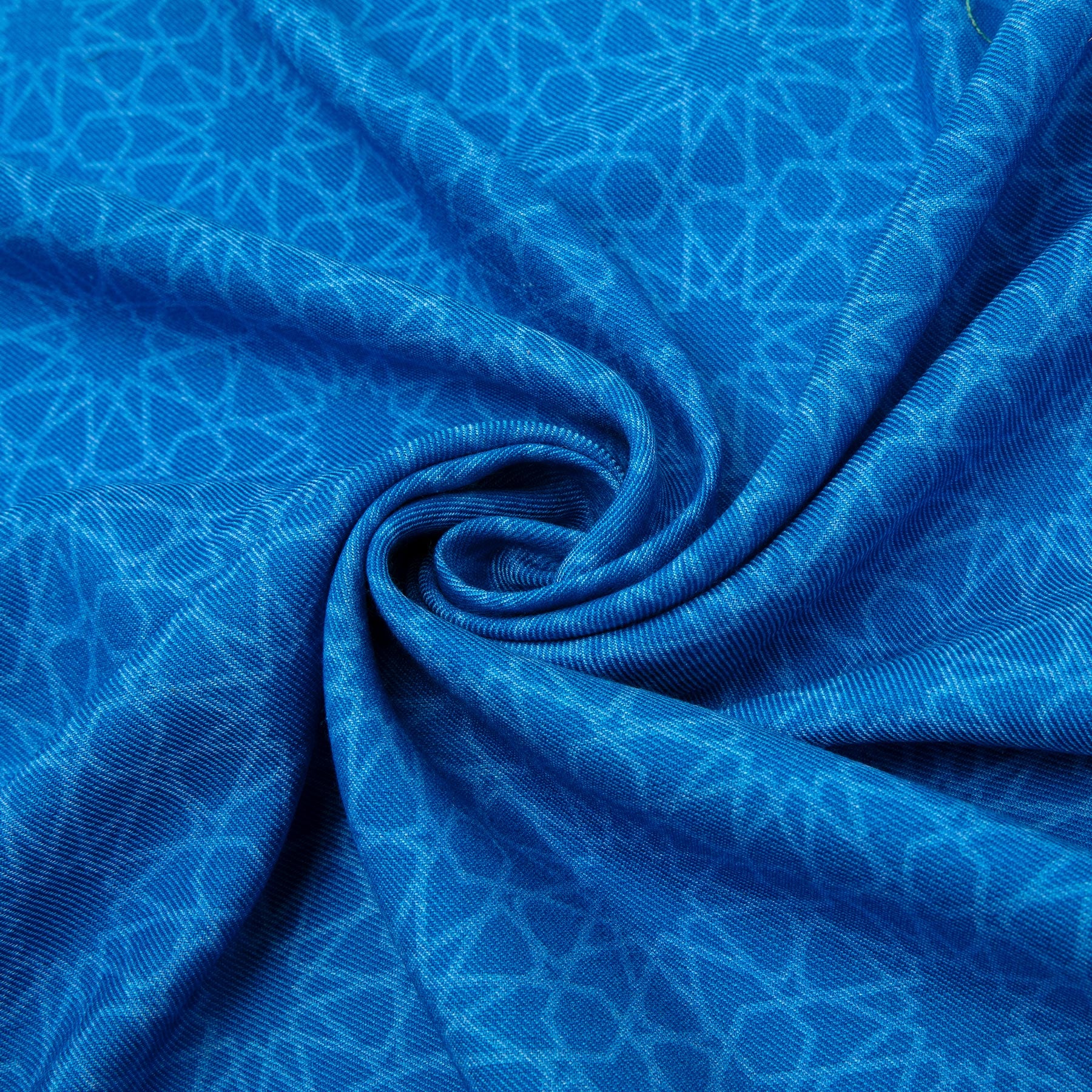 A close-up of the Hamzah Silk and Wool Blue Scarf Dalila reveals a vibrant blue fabric with a subtle geometric pattern arranged in a swirl. The silk and wool blend adds texture and an intricate design, creating depth and movement.