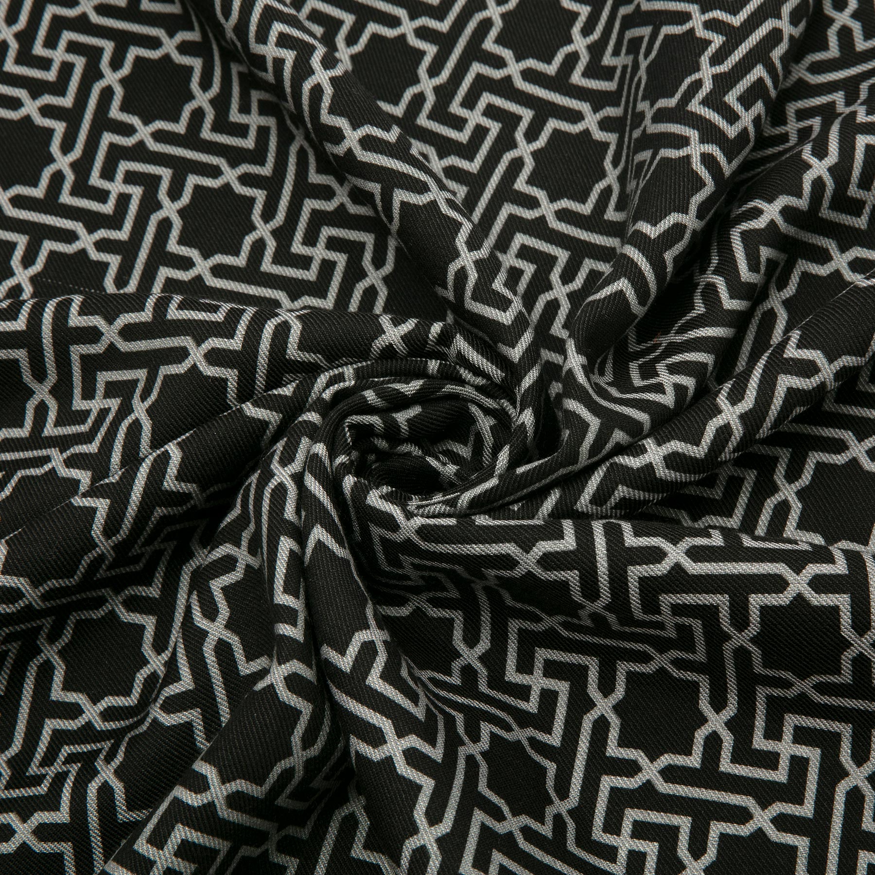 The close-up features a Hamzah Silk Wool Black and Gray Scarf Rawdah V1, with its black fabric showcasing intricate white Islamic geometric patterns, elegantly twisted to display versatile styling options and rich texture.