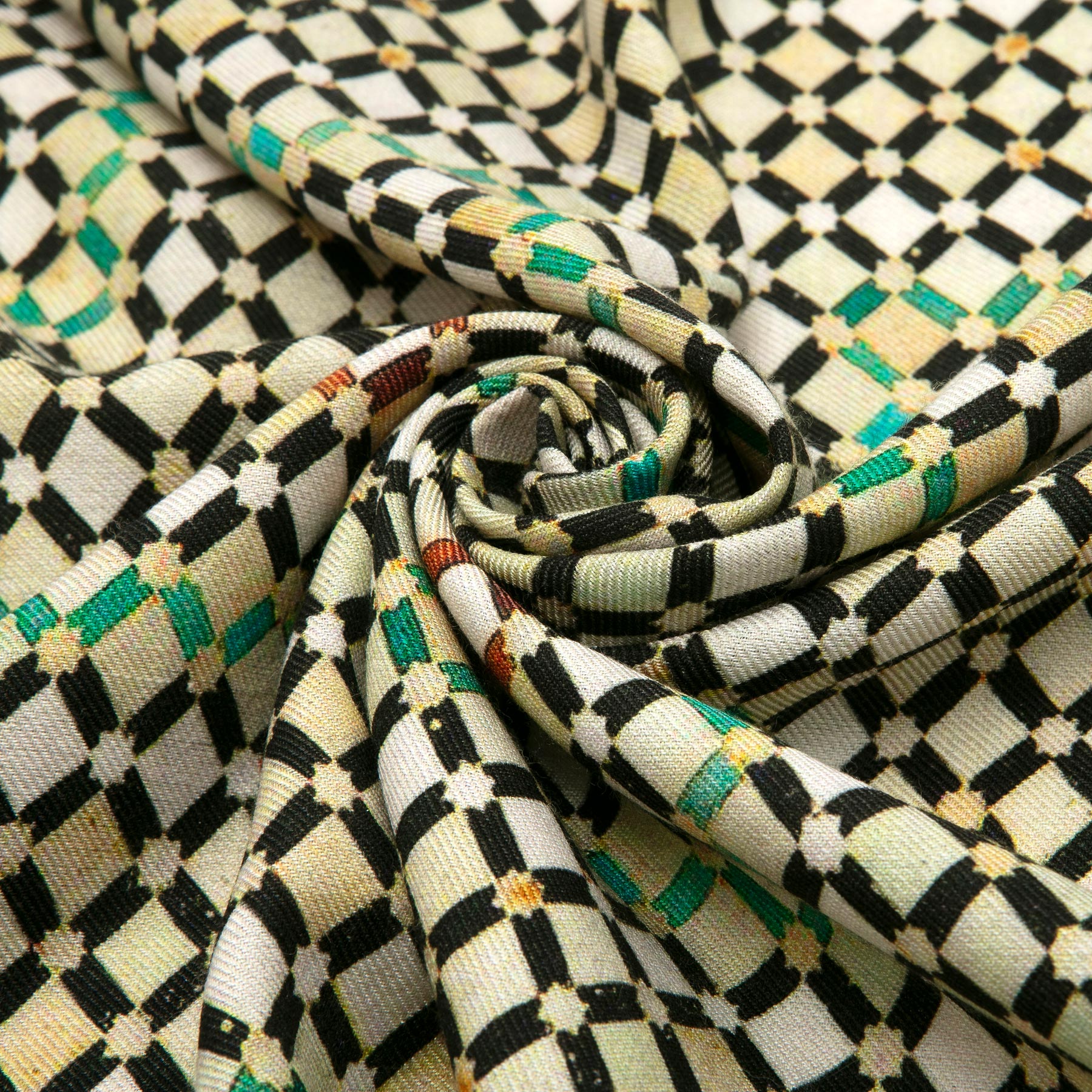 The Hamzah Silk and Wool Scarf Hub displays a close-up of its luxurious fabric, adorned with black and white squares enhanced by green and orange accents. The spiral gathers echo Islamic Arts geometric patterns, emphasizing its intricate design and rich texture.