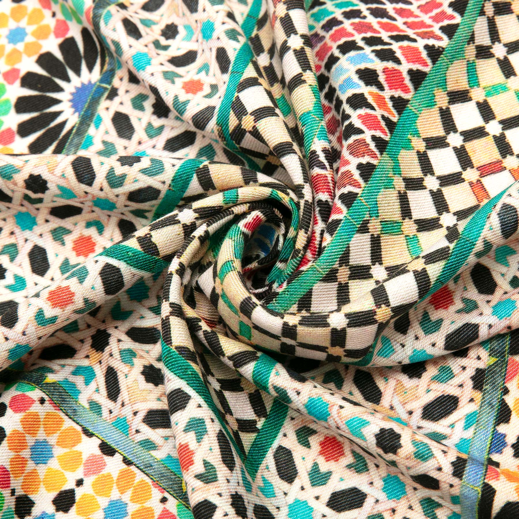 The Silk and Wool Scarf Mehdya by Hamzah features a luxurious geometric pattern inspired by Islamic art, with colorful floral and checkered designs. Twisted in the center, it showcases hues of green, black, red, and blue on a cream background.